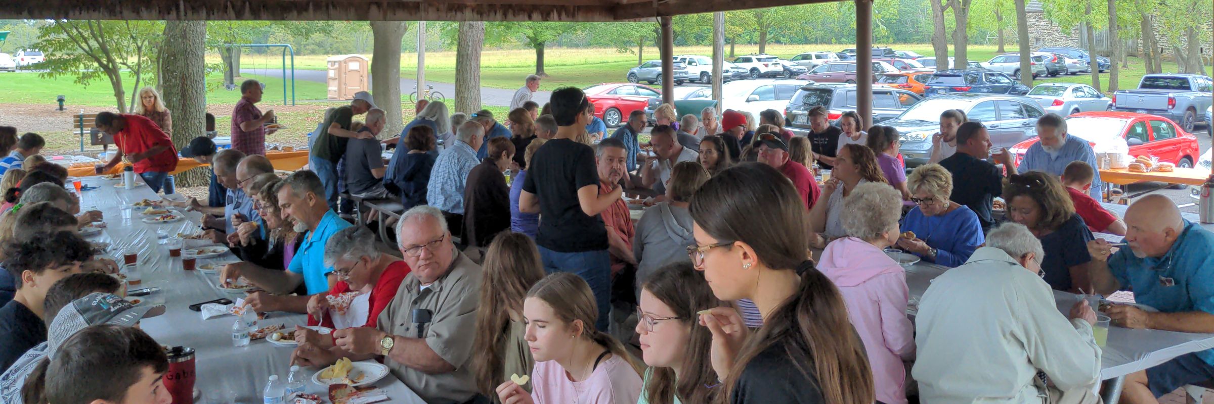 The church family sharing a meal at long tables at the 2023 church picnic