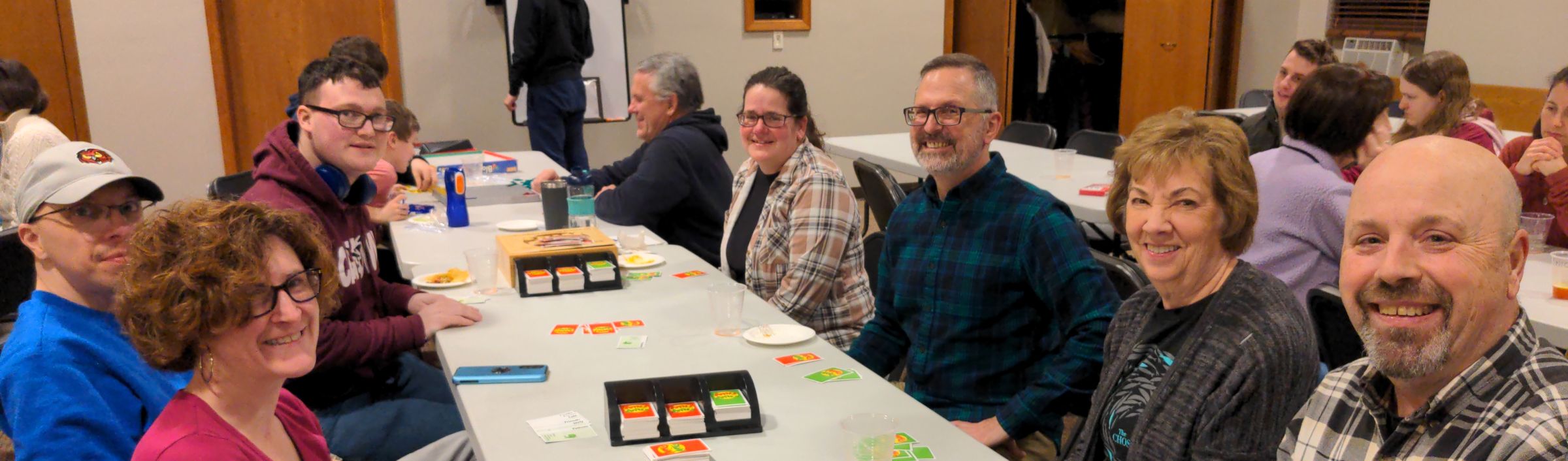 Adults playing games and smiling around a long table at church game night