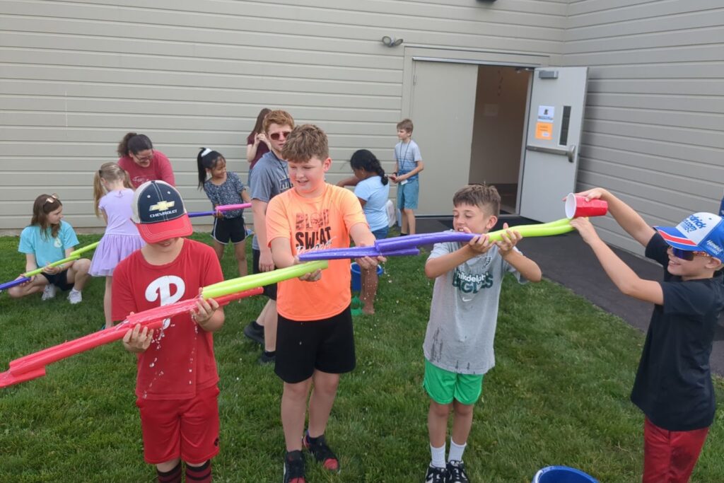 Boys passing water through pool noodles in a relay game