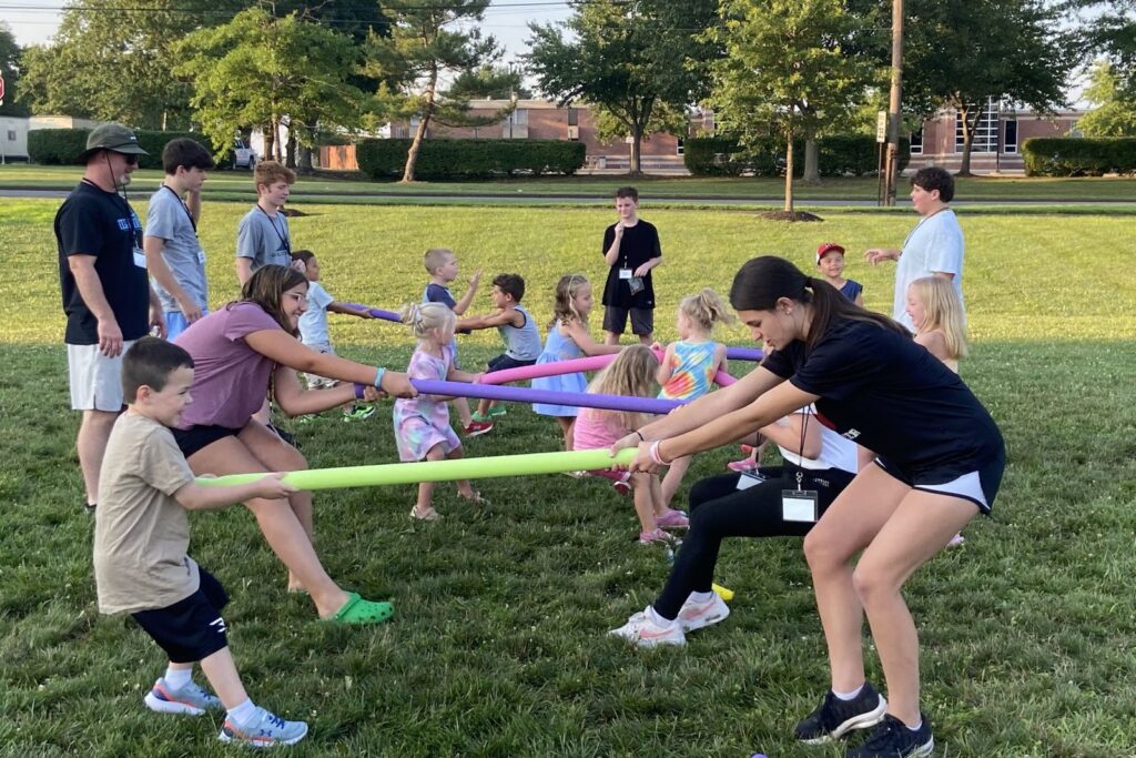 Kids and teen helpers in a pool-noodle tug of war outdoors