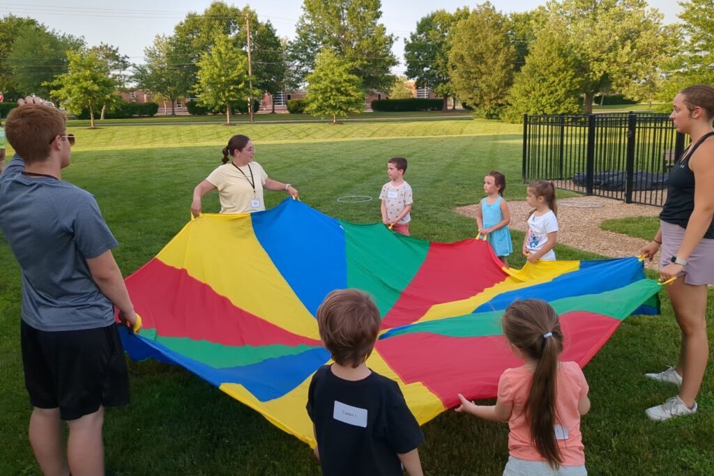 Kids and leaders playing with a rainbow parachute on the church lawn